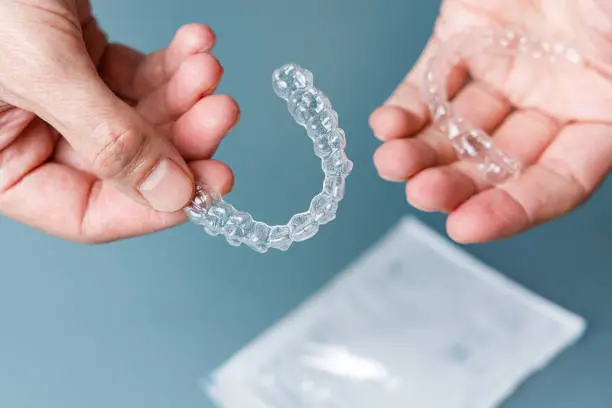 A hand holds an Invisalign clear dental aligner at Wink Orthodontics in Colleyville, TX