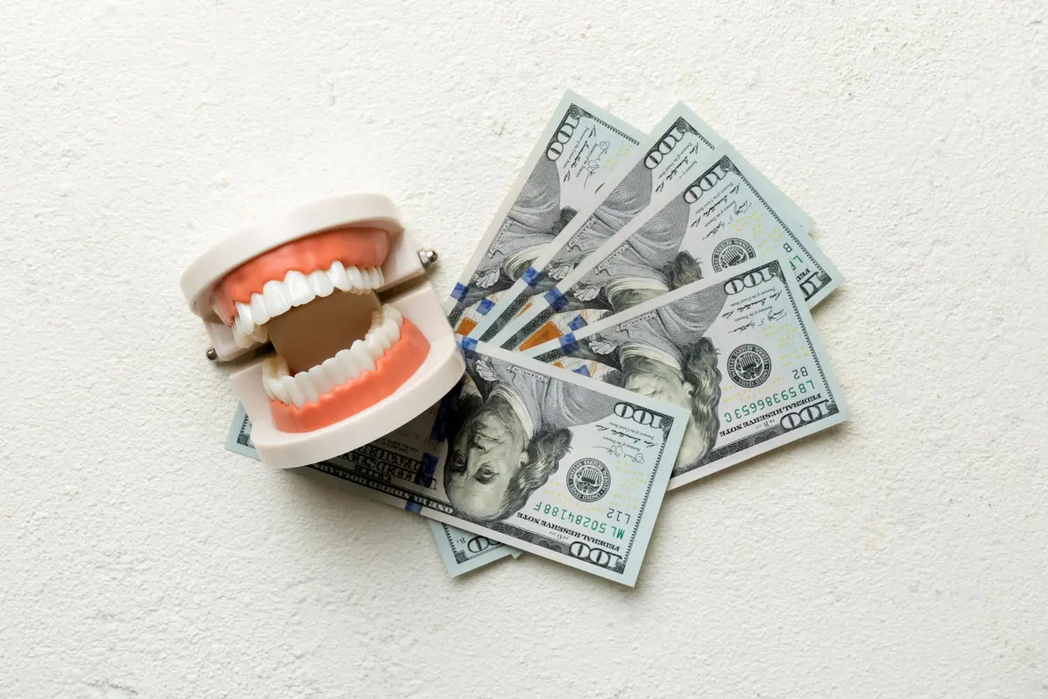 A set of artificial teeth is placed next to several US dollar bills to pay clear braces insurance at Wink Orthodontics in Prosper and Colleyville, TX
