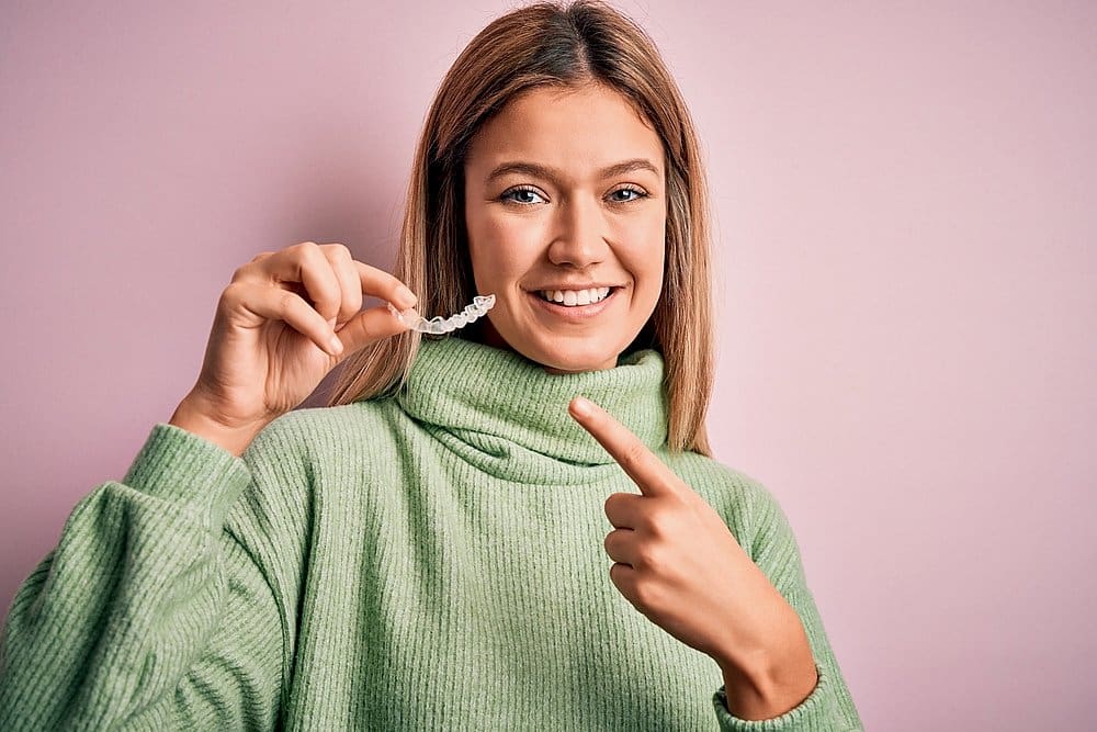 A woman in green sweater pointing at Invisalign clear aligners from Wink Orthodontics in Colleyville, TX