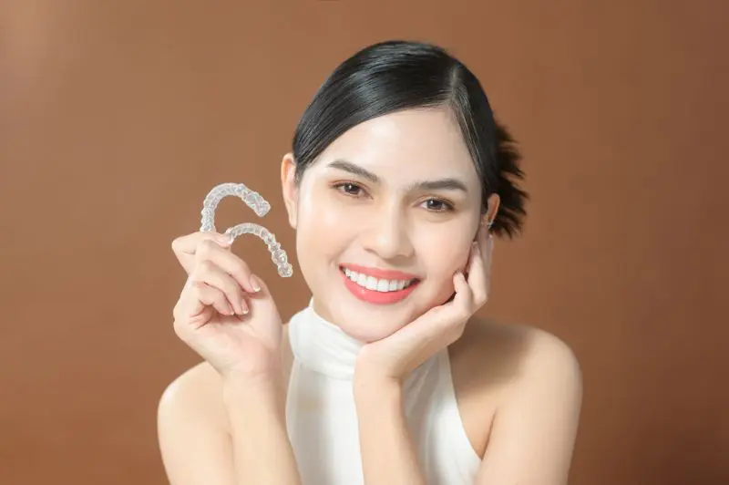 A woman smiles warmly as she holds invisalign, showcasing the best service orthodontics at Wink Orthodontics in Colleyville, TX