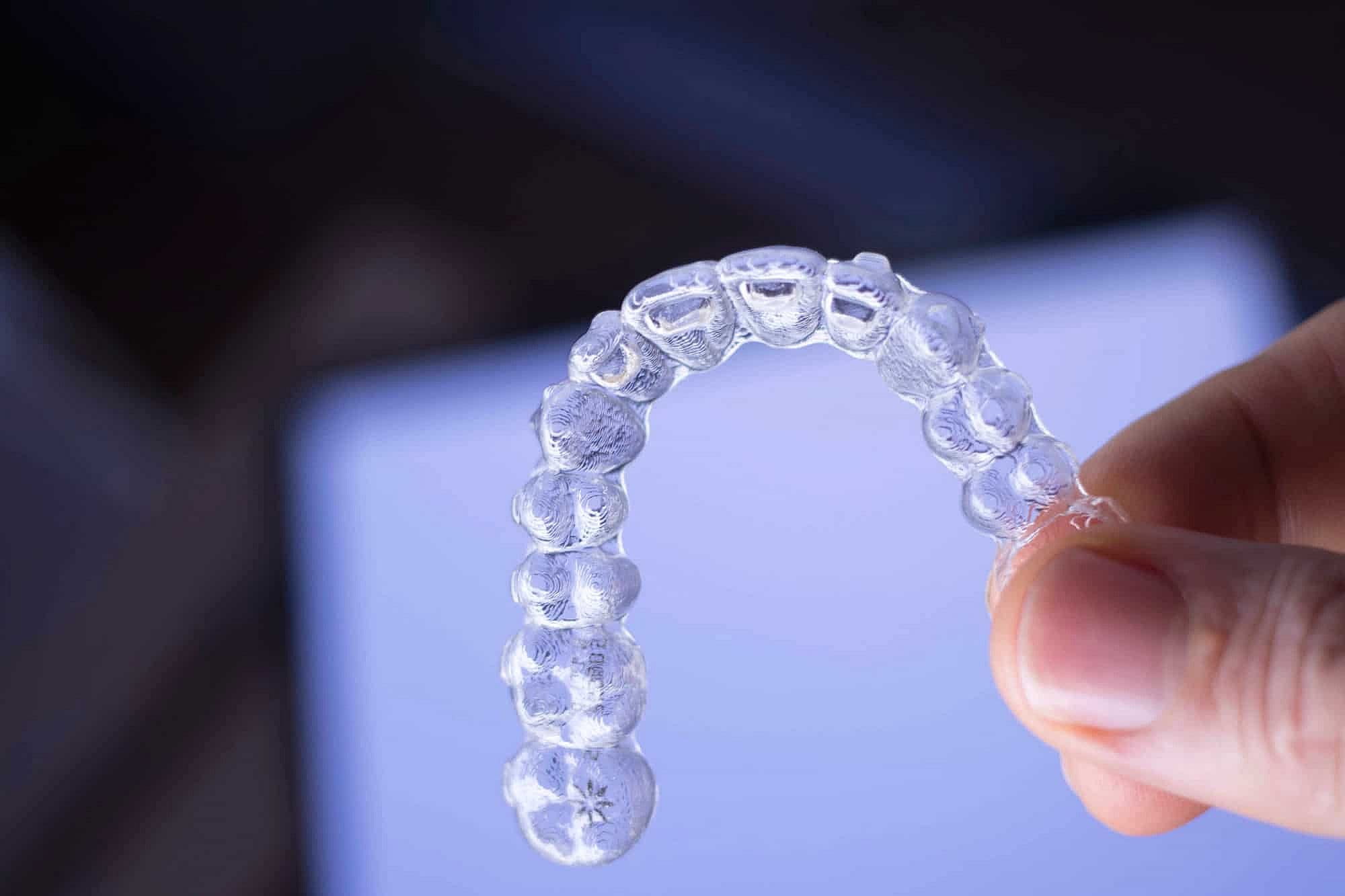A hand holding a clear dental aligner suggest choose affordable invisalign with invisalign cost   at Winks Orthodontics
in Prosper and Colleyville, TX