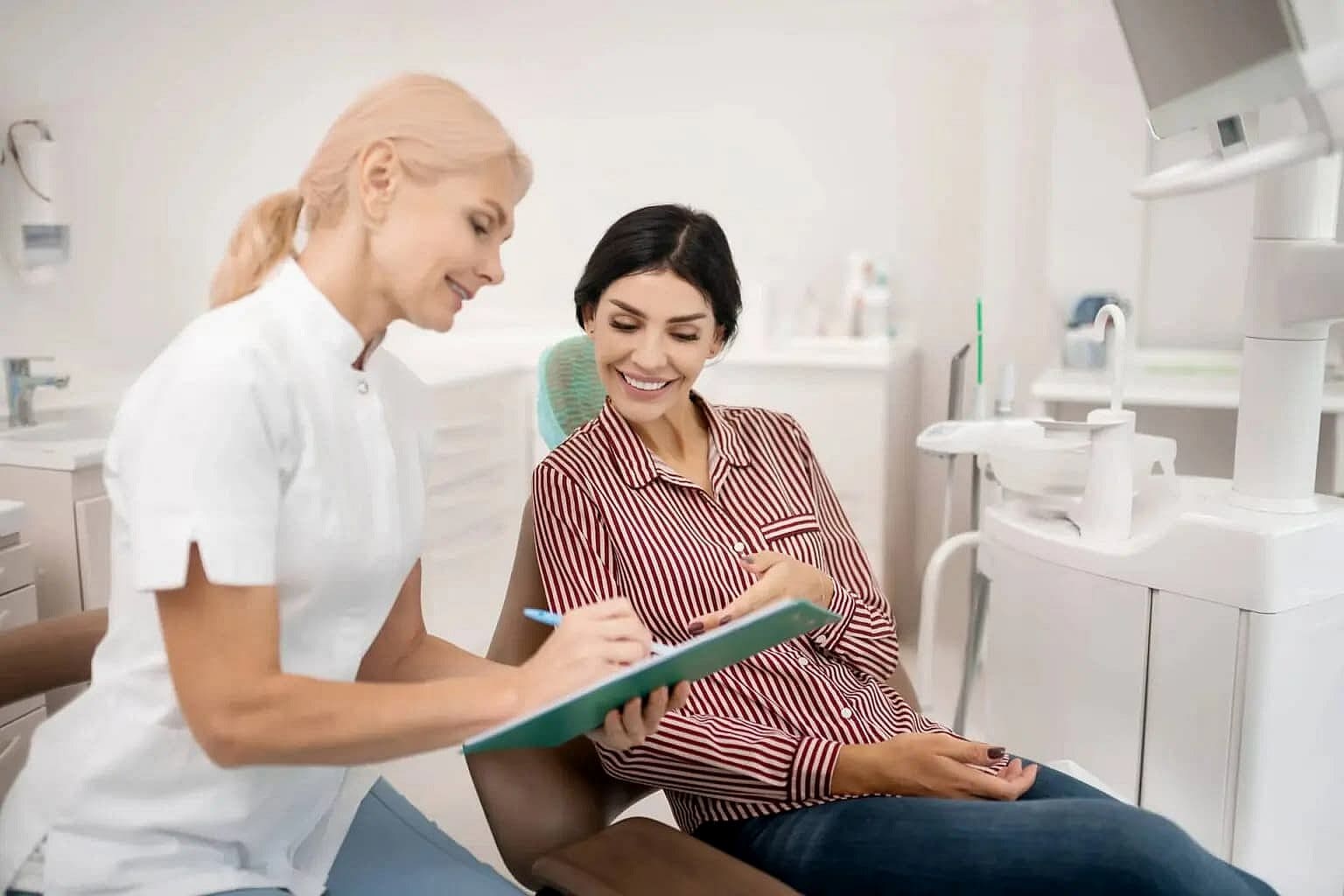 Dentist showing a clipboard to a patient seated in a dental chair, both smiling discuss about affordable invisalign cost at Wink Orthodontics in Prosper or Colleyville, TX.