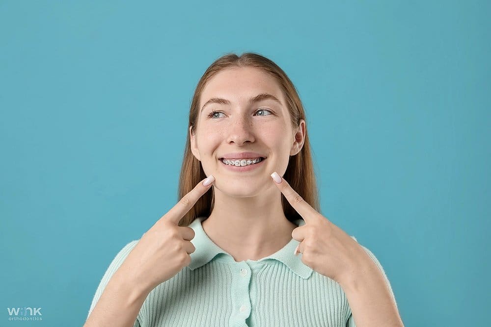 girl pointing her metal braces after understanding about how long do braces take against light blue background