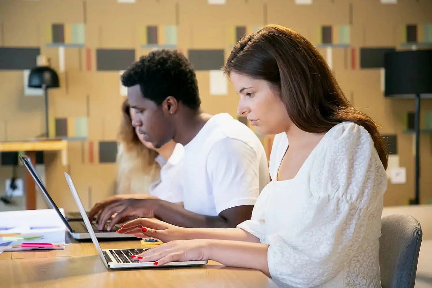 At Wink Orthodontics in Prosper or Colleyville TX, three people sit side by side at a modern, well-lit table, working on laptops while discussing affordable braces options.