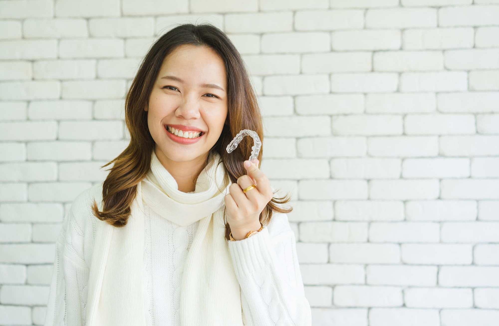 A woman smiles warmly showing an affordable Invisalign clear dental aligner, showcasing its sleek design at Wink Orthodontics in Prosper or Colleyville, TX.