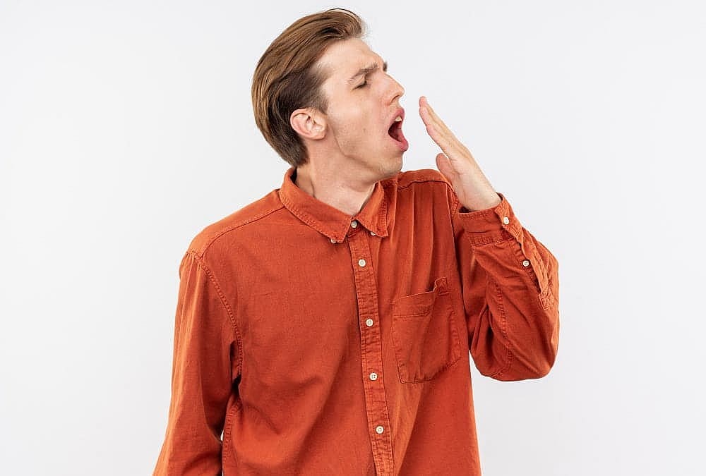 A man in an orange shirt yawns and covers his mouth, possibly mouth breathing; Wink Orthodontics in Prosper or Colleyville, TX.