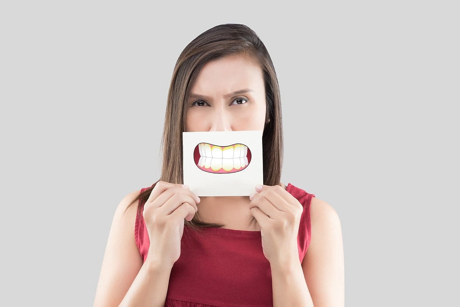 Against a gray background, a woman in red holds a smiling mouth drawing showing an underbite for Wink Orthodontics in Prosper or Colleyville, TX.