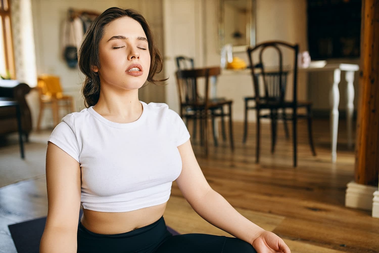 A person practicing yoga indoor, sitting cross-legged in a meditation pose, embraces tranquility as the gentle breeze offers a break from the chaos of being a mouth breather in everyday life in Prosper or Colleyville, TX