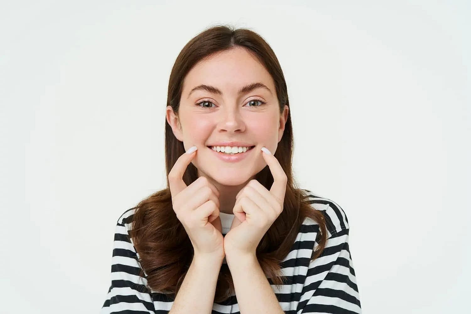 a woman smiling with her fingers on her cheeks when Overbite Treatment in Prosper or Colleyville, TX
