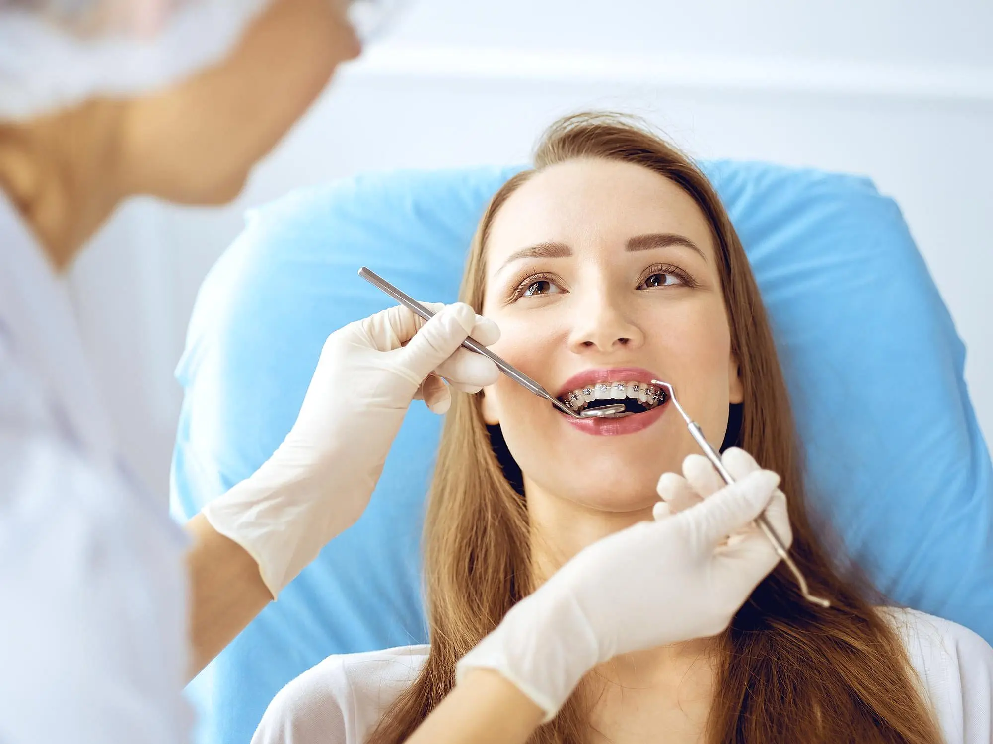 At Wink Orthodontics in Prosper, TX, a dentist uses dental tools to examine a young woman with metal braces as she sits in a blue chair.