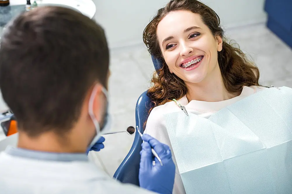At Wink Orthodontics in Prosper, TX, a young woman with braces smiles in the dental chair as she looks at her dentist during an orthodontic checkup.