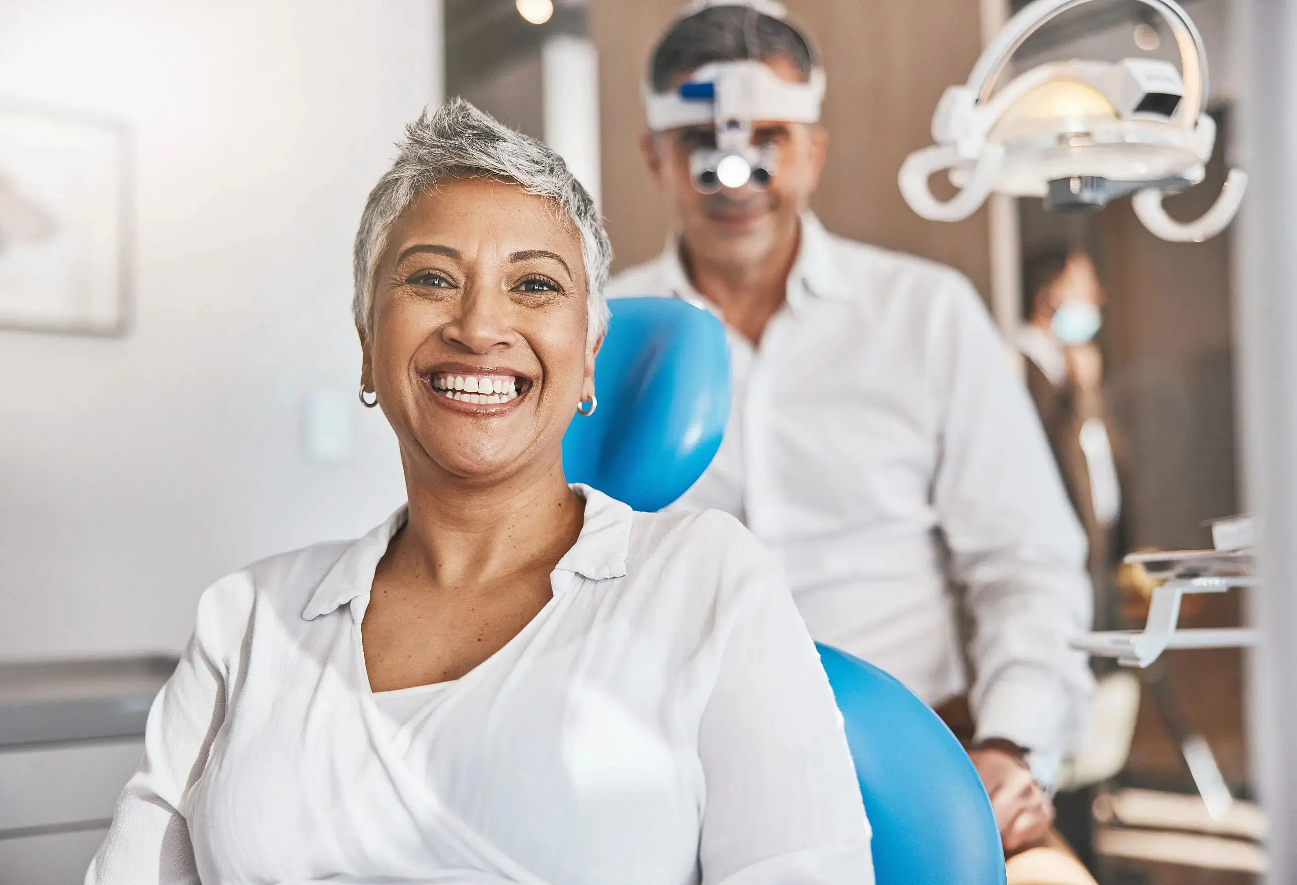 A smiling woman sits in a dental chair as a dentist stands behind her give orthodontic consultation at Wink Orthodontics in Prosper or Colleyville, TX.