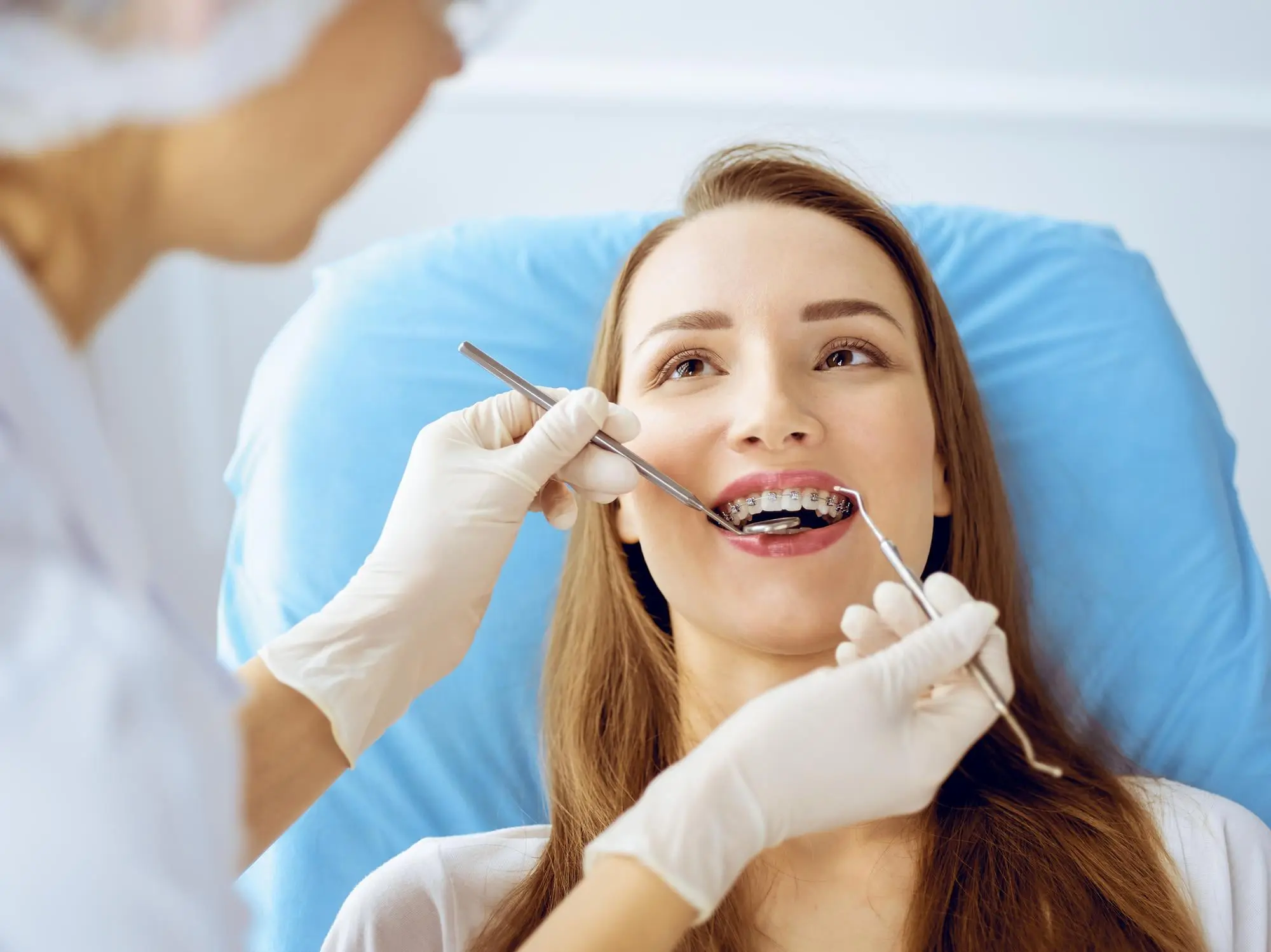 A dentist at Wink Orthodontics in Prosper or Colleyville, TX examines a young woman with braces for overbite signs in a blue chair.