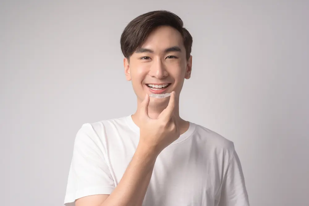 young smiling man holding invisalign clear aligners - Can Invisalign Fix Overbite in Prosper and Colleyville, TX.