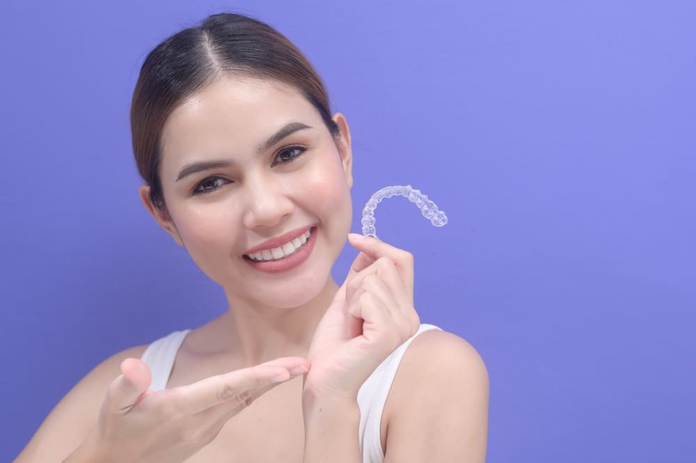 young smiling woman holding invisalign clear aligners - Can Invisalign Fix Overbite in Prosper and Colleyville, TX.