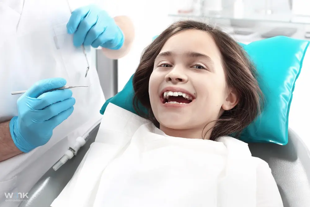 Child smiling while sitting in a dental chair, appearing happy during a dental check-up - Overbite vs Underbite in Prosper and Colleyville, TX.