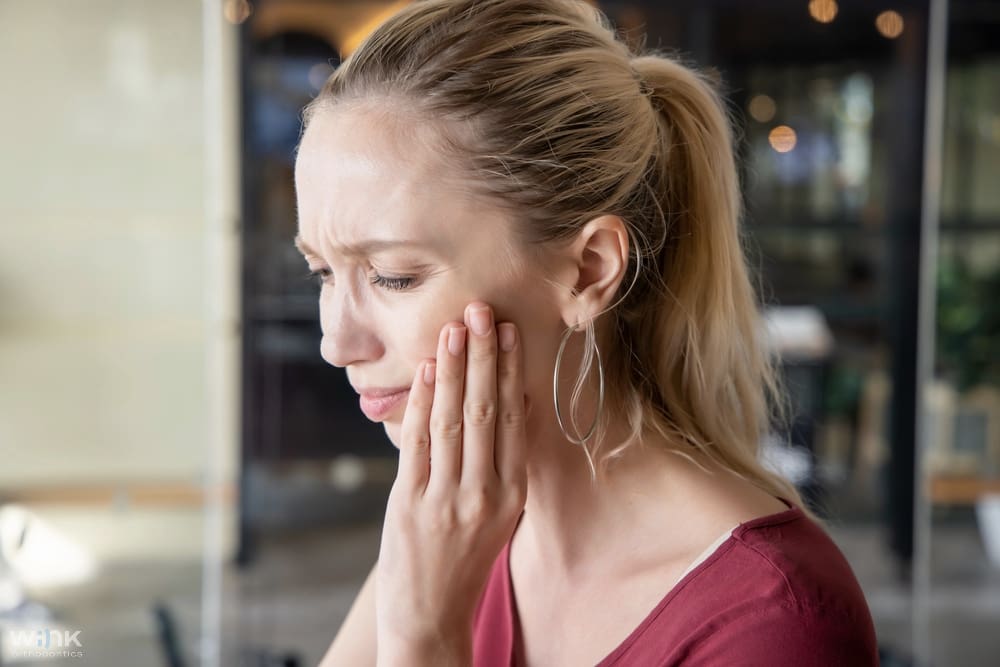 Woman touching her jaw with a pained expression, indicating jaw or tooth discomfort - TMJ Treatment in Prosper and Colleyville, TX