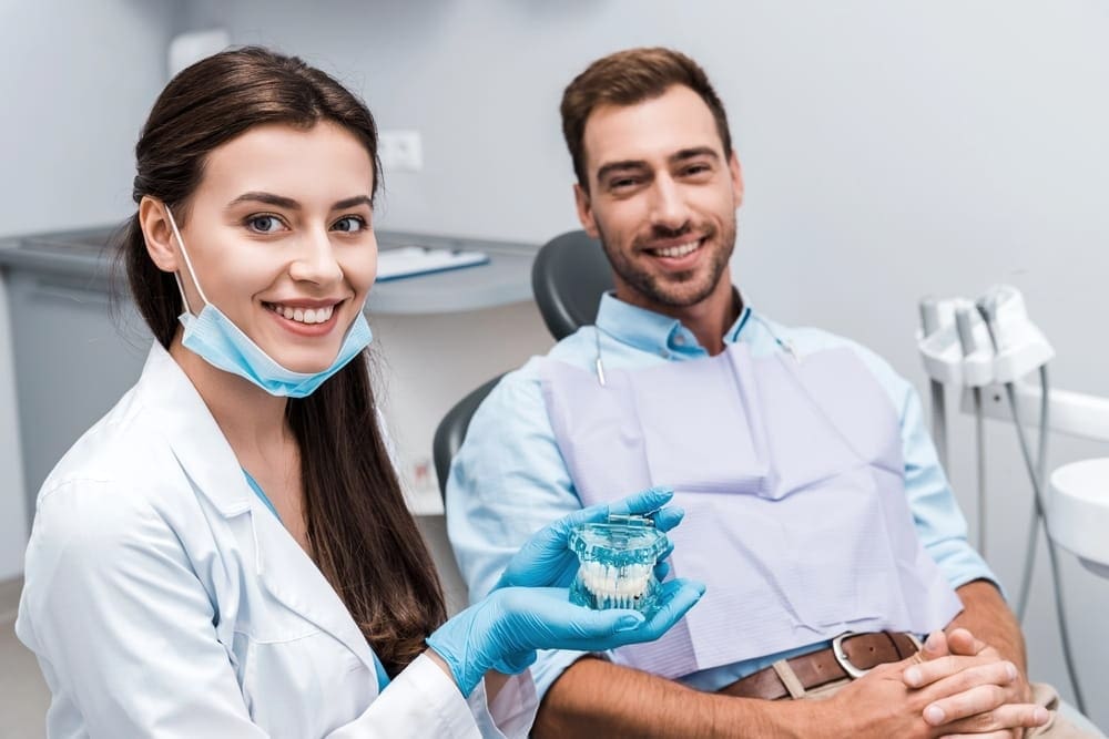 an Orthodontist in Prosper, TX holding teeth model and a patient smiling at the camera