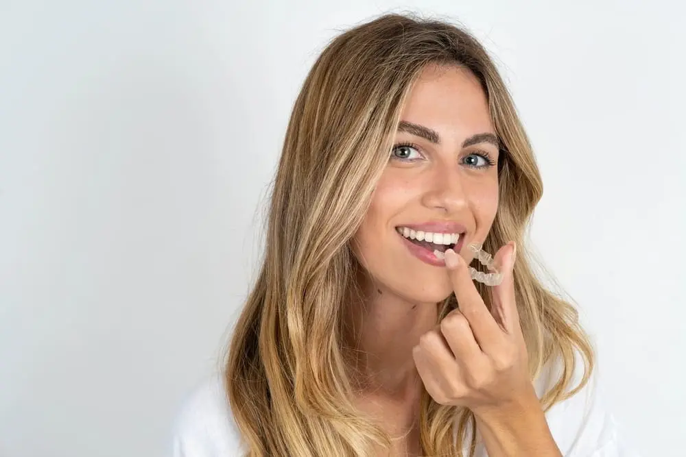 a woman smiling at the camera holding an Invisalign from an orthodontist in Colleyville, TX