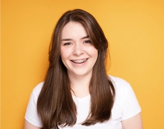 a girl standing in orang background smiling at the camera after from Orthodontist in Prosper, TX
